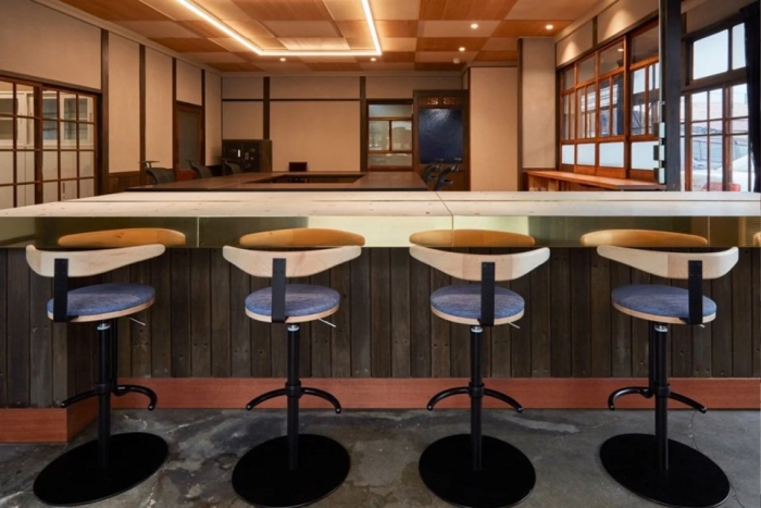 和モダンな空間が広がるカウンタースペース。古材を活かした木の温もりが感じられるデザインで、落ち着いた雰囲気を演出。背もたれ付きのカウンターチェアが4脚並び、居心地の良い空間を提供している。